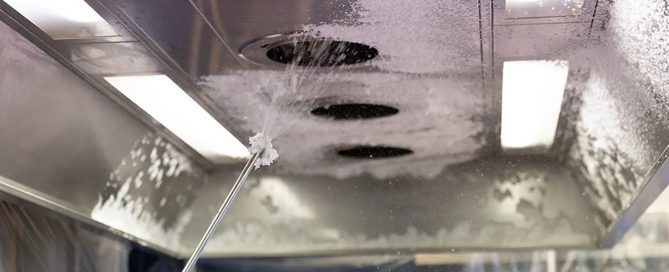 Tecnico che effettua la pulizia di una cappa industriale in cucina professionale per garantire sicurezza e igiene