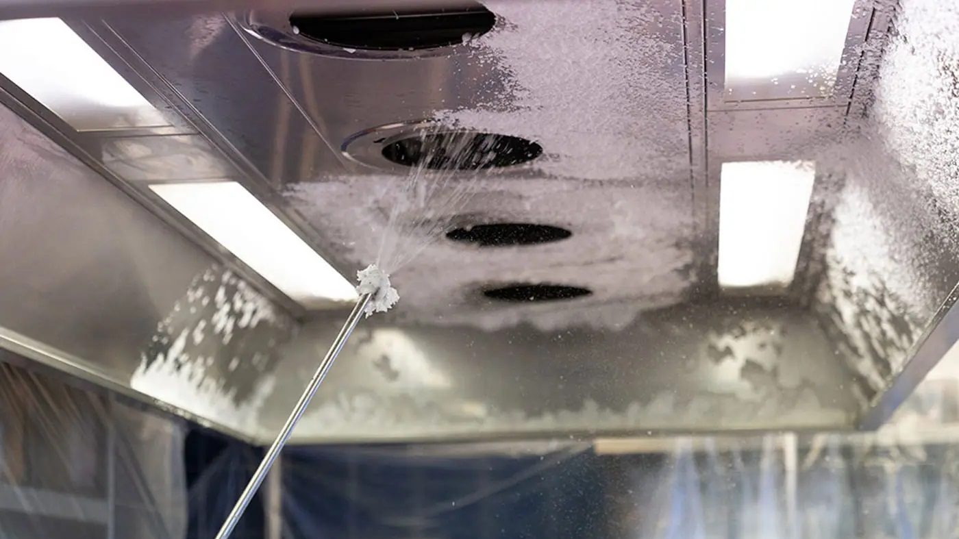 Tecnico che effettua la pulizia di una cappa industriale in cucina professionale per garantire sicurezza e igiene